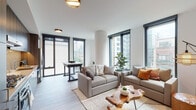Located at 845 W Madison St in Chicago's dynamic West Loop neighborhood, this well-appointed single-floor residence showcases a thoughtfully designed interior with a clean, contemporary aesthetic throughout. Large, black-framed floor-to-ceiling windows are a defining architectural feature, flooding the living spaces with natural light while offering views of the surrounding Chicago skyline.

The open living area is anchored by a generously sized seating arrangement, complete with neutral-toned sofas, warm accent pillows, and a distinctive live-edge wood coffee table that adds organic character to the modern setting. A compact dining area sits adjacent, with direct access to a private outdoor space. Light wood-style flooring runs throughout, contributing to the bright, cohesive atmosphere.

The kitchen is well-equipped with wood-grain cabinetry, stainless steel appliances including a gas range, and a geometric elongated tile backsplash that adds visual interest alongside light quartz countertops.

The bedrooms offer city views through large windows, with one room featuring a striking four-poster bed frame. Both bathrooms are finished in a clean, minimalist style — one with a glass-enclosed walk-in shower with vertical tile detailing, and another with a full tub and modern vanity.