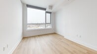 Located at 929 Richmond Rd in Ottawa's vibrant west end, this modern one-bedroom, one-bathroom unit offers a well-designed single-floor layout with clean contemporary finishes throughout. Light-toned hardwood flooring flows seamlessly across the entire space, creating a cohesive and airy atmosphere.

The open-concept kitchen and living area forms the heart of the unit. The kitchen is outfitted with sleek white cabinetry, a classic subway tile backsplash with penny-tile accents, stainless steel appliances — including a refrigerator, range, microwave, and dishwasher — and a central island with built-in shelving that doubles as a dining or prep surface. A linear pendant light overhead adds a modern finishing touch.

The bedroom is a bright, comfortable retreat featuring large floor-to-ceiling windows fitted with roller blinds, offering sweeping elevated views of the Ottawa skyline and surrounding neighbourhood. The crisp white walls and warm hardwood floors give the room a calm, minimalist character.

The bathroom is thoughtfully finished with hexagonal floor tiles, a glass-enclosed walk-in shower with white subway tile surround, a floating vanity with an integrated sink, and a full-width mirror — all presented in a clean, all-white palette.

Throughout the unit, the consistent use of white tones, natural wood, and large windows ensures excellent natural light and a sense of openness.