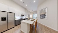 This thoughtfully designed one-bedroom, two-bathroom residence in Centennial, Colorado offers a clean, modern aesthetic throughout its efficiently organized single-floor layout. The open-concept kitchen is a standout feature, showcasing two-tone cabinetry with white uppers and charcoal lowers, sleek white quartz countertops, stainless steel appliances including a full-size refrigerator, built-in microwave, and range, and a kitchen island with bar seating — ideal for casual dining or entertaining. Light wood-style flooring flows seamlessly from the kitchen into the living area, which is bathed in natural light from a sliding glass door that opens to a private balcony. Soaring ceilings with recessed lighting and a ceiling fan enhance the airy feel of the main living space. The generously sized bedroom features plush carpet, elevated ceilings, and access to a dedicated walk-in closet. Two bathrooms serve the residence, one of which includes a full soaking tub with clean white tile surround and a gray vanity with quartz countertop. In-unit laundry is a notable convenience, with separate washer and dryer spaces each equipped with built-in shelving. The overall palette of warm neutrals and contemporary finishes creates a cohesive, inviting atmosphere throughout.