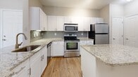 Located at 2054 Riverside Avenue in Jacksonville, FL, this efficiently designed 720-square-foot, one-bedroom, one-bathroom apartment offers a thoughtful single-floor layout with contemporary finishes throughout. The open-concept living area features warm hardwood-style flooring, crown molding, a ceiling fan with light, and a set of French doors that invite natural light and provide outdoor access. The kitchen is a standout, equipped with white shaker cabinetry, granite countertops, a subway tile backsplash, a central island, and a full suite of stainless steel appliances including a range, microwave, dishwasher, and refrigerator. The 180-square-foot primary bedroom is carpeted for comfort, includes a ceiling fan, and connects directly to a spacious walk-in closet outfitted with wire shelving on multiple levels. The bathroom continues the refined aesthetic with white cabinetry, granite countertops, and hardwood-style flooring. A dedicated laundry room houses a full-size washer and dryer with additional wire shelving above for storage. Neutral tones and consistent finishes throughout the unit create a cohesive and functional living environment.
