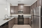 This well-designed one-bedroom, one-bathroom unit in San Antonio, Texas offers a thoughtfully organized single-floor layout that maximizes every square foot. The kitchen serves as a standout feature, boasting rich taupe cabinetry, granite countertops, stainless steel appliances including a refrigerator and microwave, a black electric range, and an integrated dishwasher. A peninsula counter with an undermount sink and elegant glass pendant lights creates a natural divide between the kitchen and living areas, adding both function and style.

Light wood-tone flooring flows consistently throughout the unit, lending a clean, cohesive look. The spacious primary bedroom is filled with natural light from dual windows dressed with white blinds and is complemented by a ceiling fan for year-round comfort. Built-in wall shelving adds a practical storage touch to the bedroom. A dedicated closet provides additional storage convenience.

The hallway connects the main living spaces to the full bathroom, which features a clean, all-white tiled tub-shower combination with chrome fixtures. The overall design palette — neutral walls, light flooring, and modern finishes — creates a bright, inviting ambiance throughout. This unit combines practical functionality with contemporary style, making it an ideal space in the heart of San Antonio.