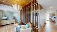 Located in Little River, South Carolina, this thoughtfully designed single-story amenity space offers a compelling blend of coastal aesthetics and functional programming. The interior is anchored by a striking lounge area defined by a dramatic floor-to-ceiling slatted wood partition accented with nautical rope detailing, creating a visual focal point that echoes the surrounding coastal environment. Warm wood plank flooring, a natural wood-paneled ceiling, and a woven shell chandelier lend the space an inviting, resort-like ambiance. Soft blue-green walls and teal accent pillows reinforce the coastal palette throughout.

The fitness center is generously equipped with a full complement of strength and cardio machines, including cable systems, treadmills, ellipticals, a rowing machine, and free weights, all reflected by floor-to-ceiling mirrors. Large windows and direct outdoor access flood the gym with natural light and views of the pool area beyond.

A dedicated co-working zone features a long built-in desk with multiple workstations, ample cabinet storage below, and a gallery-style wall of framed artwork above. Adjacent to this workspace is a well-appointed kitchenette with slate-blue cabinetry, a undermount sink, and a Starbucks coffee station, providing a convenient refresh point. Together, these areas create a versatile, amenity-rich environment suited for both active and productive use.