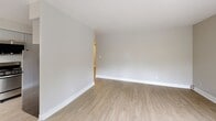 Located at 1969 SW Park Ave in Portland, Oregon, this one-bedroom, one-bathroom unit offers a practical and well-organized layout across a single floor. The entrance leads into a combined living, dining, and kitchen area that makes efficient use of the available space. The living area is brightened by a distinctive curved bay window that frames lush greenery outside, allowing abundant natural light to fill the room. Light wood-style flooring runs throughout, complementing the neutral, warm-toned walls and crisp white baseboards. Baseboard heating is present throughout the unit. The kitchen is thoughtfully updated, featuring grey shaker-style cabinetry, white countertops, a decorative penny-tile backsplash, and stainless steel appliances including a range, over-the-range microwave, and refrigerator. Ceiling fans are installed in both the kitchen and bedroom areas. The bedroom offers a comfortable footprint, a window with outdoor views, a ceiling fan with light, and access to multiple closets, including one with mirrored sliding doors. The bathroom includes a full tub and shower combination. With five closets throughout, storage is a notable feature of this unit. The overall ambiance is clean, bright, and move-in ready.