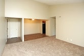 This single-story unit offers a practical and well-organized layout across several distinct areas. The main living space is notably open, featuring vaulted ceilings that lend a sense of spaciousness, with soft carpet underfoot and neutral-toned walls. A sliding glass door fills the room with natural light and provides direct access to an outdoor balcony, offering views of surrounding greenery. An adjacent area with hardwood-style flooring and a ceiling fan serves as a transitional or dining space connected via an open passage.

The bedrooms are carpeted and neutrally finished. One bedroom features a sliding closet and a textured ceiling, while another offers a sliding window that brings in natural light and outdoor views. Each room provides a comfortable, functional environment.

The kitchen is efficiently arranged in a galley-style configuration, featuring warm wood cabinetry, granite-style laminate countertops, a double stainless steel sink, and black appliances including a range and dishwasher. Wood-look flooring runs throughout this space.

The bathroom includes a tub and shower combination, rich wood-toned cabinetry with a granite-style vanity top, and dark hardwood-style flooring. A textured ceiling is present throughout most rooms, adding subtle visual character to the overall space.