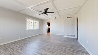This single-story unit presents a clean, modern aesthetic carried consistently throughout its layout. The main living area is a standout space, distinguished by a striking coffered ceiling with a sleek black ceiling fan, neutral gray walls, and durable wood-look luxury vinyl plank flooring that extends throughout the unit. Natural light enters through framed windows fitted with blinds, offering views of the surrounding outdoor scenery. A secondary entrance door provides convenient access directly from this area.

The kitchen is outfitted with dark navy cabinetry, white countertops, and a suite of appliances including a stainless steel dishwasher, electric range, and an over-the-range microwave, all set on matching LVP flooring.

The bedrooms are well-proportioned, each featuring neutral gray walls, LVP flooring, and natural light from windows. One bedroom is equipped with a ceiling fan, while another benefits from dual sliding-door closets with built-in shelving and hanging systems, providing ample organized storage.

The bathroom includes a full soaking tub and shower combination, a vanity with a white basin, coordinating dark cabinetry, and a privacy window. Throughout the unit, consistent finishes and thoughtful details contribute to a cohesive and functional living environment.