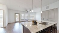 Located in Boerne, TX, this well-appointed 2-bedroom, 2-bathroom residence offers a thoughtfully designed single-level layout with a clean, modern aesthetic. The open-concept kitchen and living area serves as the heart of the home, anchored by a large granite-topped island with an undermount sink and stylish pendant lighting. Dark espresso cabinetry, matching black appliances, and wood-style flooring complete the kitchen's polished look. The living area extends toward a wall of windows and a glass door, flooding the space with natural light and providing access to the outdoors. A ceiling fan adds comfort to the airy living zone. Both bedrooms are carpeted and feature ceiling fans, generous closet space, and windows that bring in natural light. The spacious primary bedroom includes a walk-in closet with wire shelving. Each bathroom is finished with dark cabinetry, light countertops, and wood-style flooring; one features a tub-shower combination with classic white tile surround, while the other offers a separate shower. Two additional closets provide ample storage throughout. The overall palette of crisp whites and warm wood tones creates a bright, welcoming atmosphere throughout this Boerne residence.