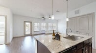 Located in Boerne, TX, this well-appointed 2-bedroom, 2-bathroom residence offers a thoughtfully designed single-level layout with a clean, modern aesthetic. The open-concept kitchen and living area serves as the heart of the home, anchored by a large granite-topped island with an undermount sink and stylish pendant lighting. Dark espresso cabinetry, matching black appliances, and wood-style flooring complete the kitchen's polished look. The living area extends toward a wall of windows and a glass door, flooding the space with natural light and providing access to the outdoors. A ceiling fan adds comfort to the airy living zone. Both bedrooms are carpeted and feature ceiling fans, generous closet space, and windows that bring in natural light. The spacious primary bedroom includes a walk-in closet with wire shelving. Each bathroom is finished with dark cabinetry, light countertops, and wood-style flooring; one features a tub-shower combination with classic white tile surround, while the other offers a separate shower. Two additional closets provide ample storage throughout. The overall palette of crisp whites and warm wood tones creates a bright, welcoming atmosphere throughout this Boerne residence.