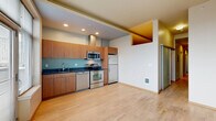 Located in the heart of Seattle's Belltown neighborhood, this 2-bedroom, 1-bathroom residence offers a thoughtfully designed layout across a single floor. The open-concept living, dining, and kitchen area serves as the heart of the home, bathed in natural light from large windows and a sliding glass door leading to a private balcony with city views. The kitchen is well-appointed with warm wood cabinetry, dark granite countertops, a tiled backsplash, and a full suite of stainless steel appliances including a refrigerator, range, dishwasher, and microwave. Light hardwood flooring flows throughout the main living areas, adding warmth and continuity to the space. A long hallway connects the living area to the two bedrooms, both carpeted for comfort. One bedroom features a tall window framing urban Seattle views, while the other offers a generous sliding-door closet. Four closets throughout the unit provide ample storage. The combined bathroom and laundry room is finished with large-format tile flooring, a wood vanity with granite countertop, and a wide mirror. The unit's clean, modern aesthetic and efficient use of space make it a practical and stylish urban residence.