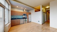 Located in the heart of Seattle's Belltown neighborhood, this 2-bedroom, 1-bathroom residence offers a thoughtfully designed layout across a single floor. The open-concept living, dining, and kitchen area serves as the heart of the home, bathed in natural light from large windows and a sliding glass door leading to a private balcony with city views. The kitchen is well-appointed with warm wood cabinetry, dark granite countertops, a tiled backsplash, and a full suite of stainless steel appliances including a refrigerator, range, dishwasher, and microwave. Light hardwood flooring flows throughout the main living areas, adding warmth and continuity to the space. A long hallway connects the living area to the two bedrooms, both carpeted for comfort. One bedroom features a tall window framing urban Seattle views, while the other offers a generous sliding-door closet. Four closets throughout the unit provide ample storage. The combined bathroom and laundry room is finished with large-format tile flooring, a wood vanity with granite countertop, and a wide mirror. The unit's clean, modern aesthetic and efficient use of space make it a practical and stylish urban residence.