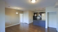 This single-floor residence offers a thoughtfully designed open-concept layout that seamlessly connects the living area and kitchen, creating a spacious and inviting atmosphere. Rich hardwood flooring flows throughout the main living space, lending warmth and continuity to the interior.

The kitchen is a standout feature, showcasing dark espresso cabinetry paired with dark granite countertops and a matching kitchen island that doubles as a breakfast bar. A set of sleek pendant lights hang above the island, providing focused task lighting and adding a contemporary touch. Black stainless steel appliances, including a refrigerator and range, complement the kitchen's modern aesthetic. A classic subway tile backsplash adds texture and visual interest behind the cooking area.

The open living space is bathed in ambient light from flush-mount and pendant ceiling fixtures, creating a bright and welcoming environment. Neutral-toned walls provide a versatile backdrop suited to a variety of décor styles. A hallway with paneled doors leads to the remaining areas of the residence, hinting at a well-organized floor plan. The overall ambiance is clean, modern, and functional, making this space well-suited for both everyday living and entertaining.