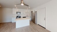 Located at 404 Encinitas Blvd in Encinitas, this single-story unit offers a clean, modern aesthetic defined by bright white walls, light wood-style luxury vinyl flooring, and recessed lighting throughout. The open-concept kitchen serves as a central feature, showcasing white shaker cabinetry with brushed nickel hardware, white quartz countertops, and a full suite of stainless steel appliances including an electric range, microwave, dishwasher, and refrigerator. A center island provides additional prep and dining space, while a dedicated walk-in pantry adds practical storage. Recessed ceiling lights and a ceiling fan enhance the kitchen and living area. The living space is bright and airy, benefiting from natural light through blinds-fitted windows with outdoor views of the surrounding neighborhood. The bedroom features its own window with natural light, a ceiling fan with integrated lighting, a wall-mounted air conditioning unit, and access to a walk-in closet. The bathroom is appointed with a frameless sliding glass shower enclosure with chrome fixtures, complementing the unit's contemporary design. Throughout, the cohesive palette of whites and light neutrals creates a fresh, welcoming ambiance.