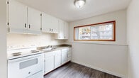This 2-bedroom, 1-bathroom single-floor unit offers a thoughtfully laid-out living space with a clean, neutral aesthetic throughout. The living room features durable hardwood-style plank flooring and a large window with warm wood trim framing, allowing natural light to fill the space. The kitchen continues the hardwood-style flooring and is equipped with white cabinetry offering generous storage, a built-in range, a double sink, and a wide window that brings in additional daylight and outdoor views. Both bedrooms are finished with plush wall-to-wall carpeting and ceiling fans with integrated lighting, providing comfort and airflow. Each bedroom includes a closet with sliding panel doors, and the unit overall benefits from an impressive five closets, ensuring exceptional storage capacity. The bathroom is finished in crisp white tones, featuring a tub-shower combination with tiled surround, a modern vanity with a clean white countertop, a framed mirror, and a small window for natural ventilation. A connecting hallway links the rooms efficiently. The unit maintains a consistently bright, neutral palette of white walls and light trim throughout, lending a fresh and move-in-ready feel to the entire space.