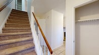 Located at 902 Gum Branch Rd in Jacksonville, North Carolina, this two-story home offers a practical and straightforward layout spread across two floors. The main level features a welcoming living room with plush carpeting, a front-facing window that invites natural light and views of the surrounding greenery, and a tiled entryway. The kitchen is equipped with white cabinetry, a double-basin stainless steel sink beneath a window, ample countertop space, and a dishwasher, providing a clean and functional workspace. A staircase with a warm wood handrail and carpeted treads connects the two floors, complemented by multiple hallways that support smooth circulation throughout the home. The full bathroom features a tub-shower combination with chrome fixtures and a white vanity with storage. Upstairs, two carpeted bedrooms offer comfortable retreats. The spacious primary bedroom includes a ceiling fan with light fixture, a window for natural light, and a built-in closet with shelving. The secondary bedroom is equally well-lit and features its own closet. Additional closet storage is available on both levels, adding to the home's practicality. The overall aesthetic is clean and neutral, with light-toned walls throughout.