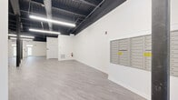 Located at 80 Cypress St in Ballston Lake, NY, this single-floor commercial space offers a clean, modern aesthetic with a highly versatile open-plan layout. The interior is defined by crisp white walls that contrast boldly against a dark-painted exposed ceiling, which showcases structural steel beams, ductwork, and linear LED lighting — a hallmark of contemporary industrial design. Light gray luxury vinyl plank flooring runs throughout the space, lending a polished yet durable finish underfoot.

The main open area is expansive and column-punctuated, providing a bright, airy atmosphere well-suited for a variety of commercial uses. A built-in multi-unit mailbox bank is mounted along one wall, indicating the space's capacity to serve multiple tenants or businesses. An elevator provides convenient vertical access, and a glass-paneled entrance door allows natural light to filter into the lobby area.

An ADA-accessible restroom is conveniently located within the space, complete with a wall-mounted sink. Additional functional elements include HVAC floor vents, a fire extinguisher, and a fire alarm system, all meeting standard commercial building safety requirements. The overall ambiance is clean, neutral, and move-in ready, offering a blank canvas ideal for office, retail, wellness, or light professional use.