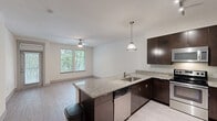 Located at 3109 Douglas Avenue in Dallas, TX, this one-bedroom, one-bathroom residence offers a well-designed, single-floor layout that maximizes every inch of its compact footprint. The open-concept kitchen anchors the living space, showcasing rich dark espresso cabinetry, granite countertops, a tile backsplash, and a full suite of stainless steel appliances including a refrigerator with ice maker, electric range, microwave, and dishwasher. A peninsula with an undermount sink and pendant lighting overhead connects the kitchen seamlessly to the living area, which features light wood-style flooring and a ceiling fan. Natural light filters through a large window with blinds, offering views of lush greenery outside. The bedroom is carpeted for comfort, features its own ceiling fan, and benefits from generous natural light through a wide double window framing outdoor foliage. A dedicated closet provides organized storage. The bathroom is finished with matching granite vanity cabinetry, large-format tile flooring, and a full tub-shower combination with white tile surround. A hallway connects the living spaces cohesively. The overall aesthetic is modern and clean, with a neutral palette throughout.