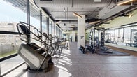 Located at 625 North 2nd Avenue in the heart of downtown Phoenix, this single-floor fitness center offers a generously proportioned exercise space designed to accommodate a full range of workout needs. The facility is defined by its floor-to-ceiling glass curtain walls that run along the perimeter, flooding the interior with abundant natural light and providing sweeping views of the Phoenix skyline and an adjacent outdoor pool area complete with lounge seating and umbrellas.

The space is organized into distinct functional zones. Along the windowed walls, a robust row of cardio machines — including treadmills, ellipticals, and stair climbers — allows users to exercise while taking in the urban scenery. A dedicated strength training area houses power racks, barbell stations, and a full complement of free weights and dumbbells, supported by wall-to-wall mirrors that enhance the sense of openness. Cable and multi-function weight machines occupy a central zone, providing versatile resistance training options.

The flooring throughout consists of durable rubber tile, well-suited for high-traffic gym use. Exposed ductwork and industrial-style linear pendant lighting contribute to the modern, urban aesthetic of the space. A standout feature is a large, colorful mural adorning one interior wall, adding an energetic and artistic focal point to the otherwise sleek, contemporary design. The overall ambiance is bright, motivating, and professionally equipped.