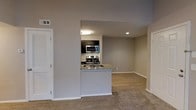 This single-floor space showcases an open-concept design that seamlessly connects the kitchen and living area, creating a cohesive and functional layout. The kitchen is appointed with dark cabinetry that contrasts attractively against light granite countertops, which extend to form a peninsula-style breakfast bar — an ideal feature for casual dining or entertaining. Stainless steel appliances, including a range, microwave, and additional cooking appliances, lend a modern aesthetic to the culinary space. The kitchen transitions into the living area through an open archway, enhancing the sense of flow and connectivity. Flooring shifts from wood-look hard surface in the kitchen to plush carpeting in the living space, adding warmth underfoot. Neutral gray walls throughout create a clean, versatile backdrop suited to a variety of décor styles. Recessed and flush-mount ceiling lighting provide consistent illumination. A louvered bifold closet door is visible near the entry, offering convenient storage. The overall ambiance is contemporary and move-in ready, with thoughtful details that balance practicality and modern style.