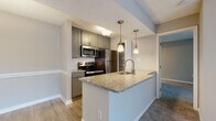 This single-floor residence in Saint Petersburg, FL offers a thoughtfully updated interior with a cohesive, modern aesthetic. The open-concept layout connects the living area, dining space, and kitchen, creating a seamless flow ideal for both everyday living and entertaining. Soft carpet covers the living and bedroom areas, while wood-look flooring runs through the kitchen and dining zone.

The kitchen serves as a functional centerpiece, featuring gray cabinetry, granite countertops, a white subway tile backsplash, and a full suite of stainless steel appliances including a refrigerator, range, and over-the-range microwave. A peninsula with an undermount sink and pendant lighting overhead provides additional workspace and casual seating. A dedicated pantry with built-in shelving adds practical storage.

The bedrooms are carpeted and well-proportioned, with one offering sliding glass door access to an outdoor area, allowing natural light to fill the space. The bathrooms mirror the kitchen's design language, with gray vanity cabinetry, granite countertops, wood-framed mirrors, and tub-shower combinations with clean white surrounds. Textured ceilings and neutral wall tones are consistent throughout, contributing to the unit's clean, move-in-ready presentation.