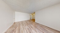 This single-floor residence offers a clean, functional layout designed for comfortable living. The main living area is spacious and open, featuring light wood-style laminate flooring and crisp white walls that create a bright, airy atmosphere. A textured ceiling adds character throughout the living spaces, while a ceiling fan provides both style and practicality. The living area connects seamlessly to a secondary space, also finished with matching flooring and a ceiling fan, offering flexibility for dining or additional lounge use. Large windows dressed with vertical blinds allow generous natural light to fill the rooms. The kitchen is efficiently designed in a U-shaped layout, featuring all-white cabinetry with black hardware, white countertops, and a built-in sink beneath a window fitted with blinds. The wood-style flooring continues into the kitchen, maintaining a cohesive look throughout the common areas. The bedroom is finished with plush neutral carpet and features a wide multi-pane window that brings in ample daylight. The full bathroom is clean and bright, equipped with a soaking tub, toilet, and a white vanity with cabinetry, accented by a window with vertical blinds. Overall, the space presents a neutral, move-in-ready aesthetic with consistent finishes throughout.