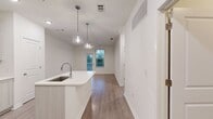 This efficiently designed 640-square-foot, single-story apartment offers 1 bedroom and 1 bathroom across a thoughtfully organized floor plan. The open-concept kitchen and living area serves as the heart of the unit, featuring light wood-tone flooring, recessed lighting, and a central kitchen island with a built-in sink and pendant lighting above. The kitchen is outfitted with white shaker-style cabinetry, white quartz countertops, and a full suite of stainless steel appliances including a refrigerator, electric range, and microwave. The living area provides direct access to a private exterior door and window, allowing for natural light and outdoor views of surrounding greenery. The 150-square-foot bedroom is carpeted for comfort and includes a ceiling fan, a large window with views of mature trees, and access to an adjacent bathroom. The bathroom features light wood-look flooring, a vanity, toilet, and a shower/tub combination. A dedicated closet provides organized storage, while the separate laundry room houses a full-size side-by-side washer and dryer with overhead wire shelving. Ceiling fans are present throughout the unit, and the clean, neutral color palette creates a bright and cohesive living environment.