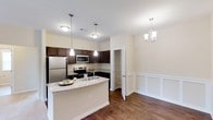 Located at 40 Stallings Mill Rd in Clayton, NC, this single-story residence showcases a thoughtfully designed open-concept layout connecting the kitchen and dining areas. The kitchen is equipped with dark espresso cabinetry that contrasts beautifully against light granite countertops, offering generous prep and storage space. A peninsula with an undermount sink serves as a natural divider between the kitchen and adjoining areas, providing additional seating and workspace. Stainless steel appliances, including a refrigerator, range, and microwave, add a contemporary touch. Pendant lighting above the peninsula and recessed lighting throughout keep the space well-lit and inviting. The adjacent dining area features classic wainscoting along the lower walls, adding architectural character, and is accented by an elegant chandelier overhead. A built-in open pantry provides convenient additional storage. Rich hardwood flooring flows seamlessly throughout both spaces, grounding the warm, neutral color palette. The overall ambiance is clean, modern, and welcoming, blending practical functionality with stylish design details.