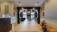 Located at 1063 Mosser Road in Breinigsville, PA, this single-floor community clubhouse offers a thoughtfully designed space for gathering, recreation, and productivity. The main entrance opens through a dramatic dark-framed archway into a soaring dining and lounge area highlighted by vaulted ceilings, an elegant chandelier, and arched windows that flood the space with natural light. Dark wood-paneled walls and light hardwood-style flooring create a bold yet welcoming contrast throughout.

The adjoining living room features a stacked stone accent wall with a built-in entertainment center, recessed lighting, a coffered ceiling, and modern furnishings that lend a sophisticated, residential feel. A separate kitchen area is equipped with dark cabinetry, granite countertops, and appliances, providing a convenient space for events and gatherings.

The spacious fitness center boasts soaring vaulted ceilings, large windows offering outdoor views, and a comprehensive array of equipment including treadmills, ellipticals, stationary bikes, and free weights, complemented by floor-to-ceiling mirrors. A business area with dark built-in shelving, a central work table, and integrated display screens rounds out the amenities, while a dedicated office nook provides additional utility for residents.