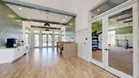 Located at 2101 Lakeview Rdg Cir in Apopka, Florida, this single-story community clubhouse offers a well-appointed gathering space with a coastal-contemporary aesthetic throughout. The airy entry foyer features soaring ceilings, light hardwood flooring, and glass-paneled double doors that flood the space with natural light and provide views of the surrounding outdoor areas, including a pool deck lined with palm trees.

The main lounge area is expansive, with floor-to-ceiling windows and direct access to the outdoor deck, creating a seamless indoor-outdoor connection. Comfortable seating arrangements, ceiling fans, and abundant natural light contribute to a bright and relaxed atmosphere.

A dedicated game room includes a statement blue billiard table set against wainscoted white walls, with a wall-mounted TV and built-in cabinetry providing both style and function. Adjacent to this is a fully equipped kitchenette featuring white shaker cabinetry, iridescent glass tile backsplash, open shelving, and stainless steel appliances.

The café-style lounge area showcases a distinctive sage green chevron shiplap accent wall, built-in booth seating, and a self-serve coffee and beverage station with a wine cooler. A fitness center with glass-panel doors and visible equipment completes this well-rounded community facility.