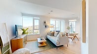 This well-appointed 2-bedroom, 2-bathroom unit is designed with a clean, contemporary aesthetic throughout. The open-concept living and dining area is anchored by large floor-to-ceiling windows that flood the space with natural light and frame stunning views of surrounding treetops and the city skyline beyond. Light wood flooring runs seamlessly throughout, complementing the bright white walls and modern furnishings.

The kitchen is a functional centrepiece, featuring two-tone cabinetry — white lower units paired with warm wood uppers — stainless steel appliances, a subway tile backsplash, and a spacious waterfall island with bar seating, ideal for casual dining or entertaining.

Both bedrooms are comfortably sized with generous natural light. The primary bedroom includes a walk-in closet and a large window offering treetop views, creating a calm and restful retreat. The second bedroom also benefits from bright window exposure. The bathrooms are finished with light, neutral materials, including wood-toned vanities and clean tile work.

A standout feature of this unit is the private balcony, accessible from the living area, offering panoramic views of the cityscape and green treetops — complete with ample space for outdoor seating. The overall ambiance is modern, airy, and inviting.