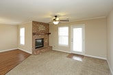 This single-floor home offers a practical and comfortable layout designed for everyday living. The living area serves as the heart of the home, anchored by a striking full-brick fireplace with a wood mantel and hearth, complemented by warm hardwood flooring, crown molding, and a ceiling fan with light fixture. Large windows with blinds allow natural light to fill the space, while a doorway provides convenient exterior access. Adjacent to the living area, the dining space features rich hardwood flooring and an elegant chandelier, opening directly into the kitchen. The kitchen is equipped with white cabinetry, light-toned countertops, a double stainless steel sink, and white appliances including a range and built-in microwave, all centered around a functional peninsula. The bedrooms are carpeted and feature ceiling fans, ample natural light, and generous closet space, including a walk-in closet in the primary bedroom. The bathrooms are finished with light tile flooring, a tub-shower combination, and a white vanity with sink. A dedicated laundry room houses a full-size washer and dryer with overhead shelving for additional storage. Throughout, neutral warm tones and consistent white trim create a cohesive and inviting atmosphere.
