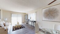 This single-floor residence offers a thoughtfully arranged layout that balances comfort and functionality across its living spaces. The open living area is bright and welcoming, featuring wood-style laminate flooring, a textured ceiling, and large windows dressed with vertical blinds that allow generous natural light to fill the room. A sliding glass door provides additional light and outdoor access. The adjoining dining area accommodates a round glass-top table and is outfitted with a ceiling fan with light fixture, contributing to a comfortable and practical atmosphere.

The galley-style kitchen features dark wood cabinetry, light countertops, tile flooring, and black appliances including a gas range and refrigerator, offering efficient use of the available space. A hallway connects the kitchen to the rest of the unit.

The primary bedroom is carpeted and well-lit by a large window with vertical blinds, offering a calm and restful environment. A second bedroom, also carpeted, includes a closet and window, suitable as a children's room or guest space.

The bathroom includes a wide vanity with dark wood cabinetry, a large mirror with overhead lighting, tile flooring, and a shower-tub combination. Overall, the residence presents a neutral, light-filled interior throughout.