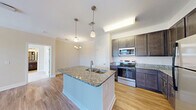 Located at 4005 Galantis Dr in Morehead City, NC, this single-floor, 2-bedroom, 2-bathroom residence offers a thoughtfully designed layout with a clean, modern aesthetic throughout. The open-concept living, dining, and kitchen area serves as the heart of the home, featuring light hardwood-style flooring, crown molding, and pendant lighting. The kitchen is well-equipped with dark cabinetry, granite countertops, stainless steel appliances, and a central island with a built-in sink — ideal for both meal preparation and casual dining. Natural light flows into the dining area through a glass door and adjacent window overlooking the outdoors. Both bedrooms are generously sized, finished with plush carpeting, ceiling fans, and multiple windows that bring in ample natural light. The spacious primary bedroom benefits from corner window placement, enhancing ventilation and views. Each bathroom features granite-topped vanities, dark wood cabinetry, and a tub-shower combination with tile surround. Additional highlights include three closets — one of which is a large walk-in with wire shelving — a dedicated pantry, a hallway, a laundry area with overhead shelving, and a welcoming entrance. This residence offers practical, comfortable living in a well-organized floor plan.
