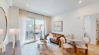 Located at 1404 Willow Ave in Hoboken, NJ, this thoughtfully designed three-bedroom, two-bathroom residence offers a bright and contemporary living experience across a single floor. The open-concept kitchen and living area serves as the heart of the home, featuring flat-front light wood cabinetry, a marble-look backsplash, quartz countertops, stainless steel appliances, and a peninsula with seating — finished with elegant gold fixtures and pendant lighting. The living room is bathed in natural light from large sliding glass doors that open to a private balcony, offering views of the surrounding Hoboken neighborhood. Light oak hardwood flooring runs consistently throughout the space, lending warmth and continuity. The primary bedroom is a comfortable retreat with bright windows and direct access to the hallway. Additional bedrooms feature large windows with outdoor views, wall-mounted lighting, and wood flooring. The two bathrooms are distinctly appointed — one with floor-to-ceiling grey tile, a walnut vanity, and gold accents, and the other with a glass-enclosed shower, large-format tile, and brushed gold hardware. Two closets provide practical storage. The overall aesthetic is clean, modern, and cohesive throughout.