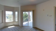 This single-floor residential space offers a welcoming and light-filled environment designed for comfortable everyday living. The main living area is finished with soft wall-to-wall carpeting that adds warmth underfoot, while neutral-toned walls create a clean, versatile backdrop throughout.

Natural light is a defining feature of this space, with multiple windows positioned to draw in sunlight from multiple angles. A prominent sliding glass door serves as both a source of abundant natural light and a direct connection to a private balcony, where a metal railing frames views of mature trees and the surrounding landscape beyond. This indoor-outdoor flow enhances the overall sense of openness and airiness.

The layout is straightforward and functional, making efficient use of the available space on a single level. The ceiling height is standard, contributing to a cozy yet comfortable atmosphere. The soft, neutral color palette throughout the living area lends itself well to a variety of furnishing styles and personal touches.

Overall, this space offers a calm and practical living environment, distinguished by its generous natural light, balcony access, and serene outdoor views — making it a pleasant retreat suited to a range of lifestyles.