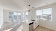 Located at 734 Wayne St in Cincinnati's 45206 neighborhood, this modern single-floor residence combines contemporary design with an abundance of natural light throughout. The open-concept kitchen serves as a central hub, featuring crisp white shaker cabinetry, gleaming white quartz countertops, a center island with an undermount sink, and a full suite of stainless steel appliances including a refrigerator, electric range, and microwave. Stylish black pendant lights hang above the island, adding a touch of contrast to the all-white palette. Light wood-look flooring extends through the main living areas, complementing the bright, airy aesthetic. The living area is bathed in natural light from expansive floor-to-ceiling windows and glass doors that open to an outdoor balcony, offering sweeping views of the surrounding Cincinnati cityscape. Two carpeted bedrooms provide a comfortable retreat, each with generous window placement that continues the home's light-filled character. Two full bathrooms mirror the home's clean design language, each appointed with white vanities, quartz countertops, and light wood-look flooring. A dedicated in-unit laundry closet with a stacked washer and dryer adds everyday convenience. The overall ambiance is clean, modern, and thoughtfully designed.