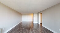 Located at 2000 Riverside Dr in Richmond, Virginia, this thoughtfully updated single-floor residence offers a clean, modern aesthetic throughout. Dark hardwood-style flooring runs consistently across the living areas and bedrooms, providing a warm contrast to the neutral gray walls and crisp white trim. The spacious living area is bathed in natural light from a full-width sliding glass door that opens to a private balcony, offering elevated outdoor views of the surrounding area. Vertical blinds provide privacy and light control. The kitchen is a standout feature, showcasing white shaker-style cabinetry with brushed nickel hardware, granite-look countertops with subtle speckled detailing, a stainless steel undermount sink, and a taupe subway tile backsplash that adds texture and depth. The bedroom includes a built-in closet with shelving and hanging rods, while an additional room with a window and baseboard heating unit provides flexibility as a second bedroom or office. The bathroom is neatly finished with a white vanity, a framed mirror, and a glass-enclosed shower. Textured ceilings and consistent finishes throughout lend a cohesive, move-in-ready feel to this well-maintained Richmond residence.