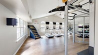 Located at 100 Antioch Pike in Nashville, TN, this fitness center is a thoughtfully designed, single-floor facility offering a comprehensive workout environment. The space is defined by its striking vaulted ceilings with exposed beams, which lend an airy, open feel throughout. Warm-toned hardwood-style flooring runs the length of the room, complementing the bright, neutral walls and creating a clean, modern aesthetic.

Natural light floods the interior through a series of large arched windows positioned along the walls, reducing the need for artificial lighting and giving the space an inviting ambiance. Pendant and ceiling-mounted lights, along with a ceiling fan, ensure the environment remains comfortable during all hours of use.

The cardio zone features a row of treadmills, a stair-climber machine, and additional aerobic equipment, each accompanied by wall-mounted flat-screen televisions for entertainment during workouts. The strength training area is equally well-appointed, with a Smith machine, cable systems, adjustable benches, barbells, weight plates, and a full rack of dumbbells. A functional training rig with pull-up bars and gymnastic rings rounds out the strength section.

Full-length mirrors line portions of the walls, enhancing the sense of space and supporting proper form during exercise. The layout is organized and spacious, allowing for fluid movement between equipment zones.