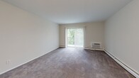 Located at 7200 Merion Trace in Upper Darby, PA, this one-bedroom, one-bathroom residence offers a practical and comfortable layout across a single floor. The living room is the heart of the unit, featuring plush wall-to-wall carpeting, neutral-toned walls, and a large sliding glass door fitted with vertical blinds that fill the space with natural light and provide access to an outdoor view of lush greenery. A wall-mounted air conditioning unit and baseboard heating ensure year-round climate comfort. The bedroom is a well-proportioned retreat, also carpeted, with a window overlooking tree-lined surroundings and generous closet space provided by two sets of sliding double-door closets — offering abundant storage. The bathroom is clean and functional, featuring white cabinetry, a white countertop vanity with a classic chrome faucet, a large mirror, and white tile wainscoting along the walls. Wood-look flooring in the entryway and bathroom adds a warm contrast to the carpeted living areas. The overall aesthetic is bright, neutral, and move-in ready, making this unit a practical choice for those seeking comfortable living in Upper Darby.