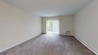 Located at 7200 Merion Trace in Upper Darby, PA, this one-bedroom, one-bathroom residence offers a practical and comfortable layout across a single floor. The living room is the heart of the unit, featuring plush wall-to-wall carpeting, neutral-toned walls, and a large sliding glass door fitted with vertical blinds that fill the space with natural light and provide access to an outdoor view of lush greenery. A wall-mounted air conditioning unit and baseboard heating ensure year-round climate comfort. The bedroom is a well-proportioned retreat, also carpeted, with a window overlooking tree-lined surroundings and generous closet space provided by two sets of sliding double-door closets — offering abundant storage. The bathroom is clean and functional, featuring white cabinetry, a white countertop vanity with a classic chrome faucet, a large mirror, and white tile wainscoting along the walls. Wood-look flooring in the entryway and bathroom adds a warm contrast to the carpeted living areas. The overall aesthetic is bright, neutral, and move-in ready, making this unit a practical choice for those seeking comfortable living in Upper Darby.