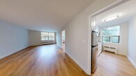 This 2-bedroom, 1-bathroom unit is thoughtfully laid out across a single floor, offering a clean, functional living environment with a warm and inviting aesthetic throughout. Warm-toned hardwood flooring runs continuously through every room, providing a cohesive and polished look.

The living area is spacious and bright, benefiting from large windows that frame outdoor views and allow generous natural light to fill the room. A radiator beneath the window provides efficient heating. The space flows naturally into a hallway that connects the main living areas to the bedrooms.

The kitchen is well-equipped with white cabinetry, light countertops, a tile backsplash, and stainless steel appliances including an electric range, over-the-range microwave, and refrigerator. A window over the cooking area brings in additional natural light and garden views.

The generously sized primary bedroom offers ample space and includes a closet. The second bedroom is also well-proportioned, featuring its own closet and access to the hallway. Both rooms maintain the same warm hardwood flooring found throughout the unit.

The bathroom is clean and simply finished, featuring a full bathtub with white subway tile surround. An entrance and hallway complete the layout, offering a practical transition into the main living spaces.