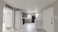 This single-floor unit offers a practical and well-organized layout, as revealed by the overhead floor plan view. The kitchen serves as a central feature of the space, designed with gray shaker-style cabinetry offering ample storage both above and below the countertops. A classic white subway tile backsplash adds a clean, timeless aesthetic, complemented by light countertops and a double-basin stainless steel sink positioned beneath a window fitted with vertical blinds, allowing natural light to filter in. Black appliances, including a gas range with overhead ventilation and a full-size refrigerator, provide functional contrast to the lighter cabinetry. A small open shelving unit acts as a partial divider, adding modest storage and subtle definition between the kitchen and adjacent living areas. Light wood-look flooring runs throughout the unit, contributing to a cohesive, airy feel. The bedroom is a well-proportioned room featuring the same light flooring and a large window with vertical blinds, offering natural light and an outward view. The bathroom is finished with white square wall tiles, light tile flooring, a combination tub and shower, and brushed nickel fixtures, maintaining a clean and neutral aesthetic throughout.