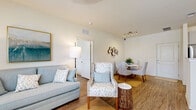 This thoughtfully designed 2-bedroom, 1-bathroom residence offers a comfortable and cohesive living experience across a single floor. Wood-look flooring runs throughout the home, tying together a warm, neutral palette complemented by crisp white walls and abundant natural light streaming through large windows dressed with blinds and flowing drapes.

The living room provides a welcoming gathering space, featuring large windows that invite outdoor views and ample room for relaxed seating arrangements. It flows naturally into a dedicated dining area, which is illuminated by stylish track lighting and offers an intimate setting for everyday meals. The adjacent kitchen is well-equipped with white shaker cabinetry, granite-style countertops, and a full suite of stainless steel appliances, including a refrigerator, range, and over-the-range microwave.

The primary bedroom is generously sized, accommodating a full furniture arrangement with ease. It includes a ceiling fan, a large window with outdoor views, and access to a walk-in closet outfitted with wire shelving and a tufted bench. The second bedroom offers a comfortable and private retreat. The shared bathroom features a granite-topped vanity with shaker-style cabinetry and a full tub-shower combination. The overall ambiance is light, airy, and move-in ready.