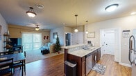 Located at 2807 Bobcat Dr in Ames, Iowa, this well-appointed single-floor residence offers a thoughtfully designed layout across one bedroom, one bathroom, a combined kitchen and living room, a closet, and a hallway. The open-concept kitchen and living area forms the heart of the home, showcasing rich dark-stained cabinetry, granite countertops, and a central island with bar seating for two — illuminated by elegant pendant lighting overhead. Stainless steel appliances, including a refrigerator, electric range, and microwave, complete the kitchen. Warm hardwood-style flooring runs throughout the kitchen and entry areas, while the living room transitions to plush carpet underfoot. The living room features a ceiling fan, sliding glass door access to the outdoors, and a comfortable, open atmosphere. The generously sized bedroom is carpeted, offers ample natural light through a window, and is fitted with a ceiling fan. The full bathroom includes a single-sink vanity with dark wood cabinetry, a sliding-door walk-in shower, and tile flooring. A dedicated closet and hallway round out the floor plan, providing practical storage and connectivity between spaces. The overall design is clean, modern, and functional.