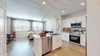 This thoughtfully designed single-story residence offers a seamless open-concept layout connecting the kitchen, dining, and living areas, all unified by light-toned hardwood-style flooring throughout. The modern kitchen serves as a central hub, featuring a granite-topped island with an undermount sink and dishwasher, crisp white shaker cabinetry, stone countertops, and a full suite of stainless steel appliances including a range, microwave, and refrigerator. The living room is bright and welcoming, with multiple windows dressed in soft linen blinds and a ceiling fan overhead. A hallway leads to the private bedroom, a comfortably sized retreat with a large window, hardwood-style flooring, and direct access to a spacious walk-in closet outfitted with wire shelving and hanging rods. The bathroom is elegantly finished with a granite vanity, wood-toned flooring, and a full tub-shower combination surrounded by marble-look tile surround. Recessed lighting and a clean, neutral color palette lend a bright, airy ambiance throughout the entire residence, making it a functional and stylish living space.