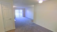 This single-floor residential space offers a clean, functional layout with a welcoming and practical design. The main living area is finished with wall-to-wall carpeting in a neutral tone, providing a comfortable and quiet underfoot experience throughout. Smooth, light-colored walls create a bright and open atmosphere, contributing to the airy feel of the space.

A prominent sliding glass door fitted with vertical blinds serves as both a natural light source and a connection to the outdoors, allowing sunlight to filter into the living area and enhancing the sense of openness. A ceiling-mounted fan and light fixture provides overhead illumination and air circulation, adding to the room's everyday comfort.

The textured ceiling adds a subtle architectural detail consistent with classic residential construction. The open layout of the living area allows for flexible furniture arrangements, making it easy to personalize the space to suit a variety of lifestyles. Overall, the space presents a straightforward and livable environment with practical finishes and a light, neutral palette throughout.