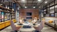 Located at 1201 Constitution Ave in Philadelphia, PA, this single-floor communal space delivers a refined industrial-chic aesthetic across three thoughtfully designed areas. The layout transitions seamlessly from a polished concrete entryway — anchored by an elevator bank and clean gray walls — into a series of sophisticated lounge zones.

The primary lounge is the visual centerpiece, featuring a dramatic floor-to-ceiling reclaimed wood accent wall with a wall-mounted flat-screen TV and a sleek linear fireplace at its base. Swivel chairs in warm blush tones are arranged around a round white coffee table atop a textured area rug, creating an inviting conversation setting. Open black steel shelving units display curated decorative objects alongside warm wood cabinetry, adding depth and character.

A black steel grid ceiling framework carries pendant and track lighting throughout, lending the space an open, loft-like industrial quality. A secondary lounge corridor transitions toward large glass windows and doors that offer views of an exterior courtyard, with bold, large-scale abstract paintings in vivid pinks, teals, and yellows adorning the gray walls. Additional seating with accent tables provides a quieter nook within this zone.

Together, the three areas form a cohesive, design-forward environment that balances comfort with contemporary style.