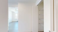 This thoughtfully designed one-bedroom, one-bathroom unit offers a clean, modern aesthetic defined by an all-white palette, light-toned wide-plank laminate flooring, and an abundance of natural light. The open-concept living and kitchen area is anchored by a dramatic wall of floor-to-ceiling windows, framing expansive panoramic views that flood the space with daylight and create a sense of openness well beyond the unit's compact footprint.

The kitchen is efficiently designed with a two-tone cabinetry scheme — crisp white upper cabinets paired with warm wood-grain lower cabinets — complemented by a white subway tile backsplash and light quartz countertops. A full suite of stainless steel appliances, including a built-in microwave, electric range, dishwasher, and bottom-mount refrigerator, provides complete functionality.

The bedroom is a well-proportioned, serene retreat with access to a private balcony through a full-height sliding glass door, allowing natural light to pour in. Baseboard heating ensures year-round comfort.

The bathroom is finished in a clean, spa-like style featuring large-format white wall tiles, a soaker tub with overhead shower, a sleek vanity with stone countertop, and a large mirror. Recessed lighting and textured flooring complete the polished look. Overall, the unit presents a bright, contemporary living environment with a cohesive modern design language.