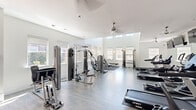 This fitness center at 5400 Walkertown Landing Cir offers a generously sized, single-floor workout facility designed to accommodate a full range of exercise needs. The space is defined by its clean, contemporary aesthetic, with crisp white walls, light wood-style flooring, and an open layout that promotes ease of movement throughout.

Soaring ceilings with clerestory windows along the upper walls flood the interior with abundant natural light, creating a bright and energizing atmosphere. Ceiling fans are strategically placed throughout to ensure comfortable airflow during workouts. Recessed lighting supplements the natural illumination for a well-lit environment at all hours.

The facility is comprehensively outfitted with a variety of Spirit-brand treadmills, elliptical machines, stationary bikes, and multi-function cable and strength training machines, offering robust options for both cardio and resistance training. Wall-mounted mirrors along one side visually expand the space and support form-checking during exercise. Multiple flat-screen televisions are mounted on the walls for entertainment convenience.

Large windows along the perimeter provide outdoor views and reinforce the open, airy feel of the space. A glass-panel entryway connects to an adjacent area, and a secured exterior door provides direct outdoor access. The overall ambiance is modern, clean, and functional — a well-maintained facility suited for serious fitness routines.