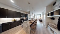 This thoughtfully designed single-floor residence offers a seamless blend of modern aesthetics and functional living. The heart of the home is an open-concept kitchen and living area, where dark espresso cabinetry contrasts beautifully with light granite countertops along a generous island that doubles as a breakfast bar with seating. Stainless steel appliances and a subway tile backsplash complete the chef-inspired kitchen, while pendant lighting adds a sophisticated touch overhead. The living room flows naturally from the kitchen, bathed in natural light from large windows dressed with floor-length drapes. A ceiling fan, light wood-look flooring, and a neutral palette create a calm, inviting atmosphere. The primary bedroom is a serene retreat, featuring plush carpet, oversized windows, and curated wall art. Its en-suite bathroom impresses with a dual-sink granite vanity, dark cabinetry, wood-look flooring, and direct access to a walk-in closet with built-in shelving. A second bedroom mirrors the same refined comfort with large windows and soft tones. A dedicated entryway with open shelving and coat hooks provides convenient everyday organization. Throughout the residence, cohesive finishes and modern design elements create a polished, welcoming environment.