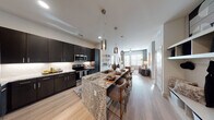 This thoughtfully designed single-floor residence offers a seamless blend of modern aesthetics and functional living. The heart of the home is an open-concept kitchen and living area, where dark espresso cabinetry contrasts beautifully with light granite countertops along a generous island that doubles as a breakfast bar with seating. Stainless steel appliances and a subway tile backsplash complete the chef-inspired kitchen, while pendant lighting adds a sophisticated touch overhead. The living room flows naturally from the kitchen, bathed in natural light from large windows dressed with floor-length drapes. A ceiling fan, light wood-look flooring, and a neutral palette create a calm, inviting atmosphere. The primary bedroom is a serene retreat, featuring plush carpet, oversized windows, and curated wall art. Its en-suite bathroom impresses with a dual-sink granite vanity, dark cabinetry, wood-look flooring, and direct access to a walk-in closet with built-in shelving. A second bedroom mirrors the same refined comfort with large windows and soft tones. A dedicated entryway with open shelving and coat hooks provides convenient everyday organization. Throughout the residence, cohesive finishes and modern design elements create a polished, welcoming environment.