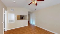 This single-floor residence offers a well-organized layout with consistent warm-toned hardwood-style flooring flowing throughout every room, creating a cohesive and inviting atmosphere. The living room serves as the heart of the home, highlighted by vaulted ceilings, a ceiling fan with light fixture, and a classic tile-surround fireplace that anchors the space. Natural light filters in through multiple windows fitted with blinds, while a sliding glass door with vertical blinds provides access to the outdoors. A pass-through window connects the living area to the kitchen, enhancing the open feel. The kitchen is efficiently designed with dark cabinetry, granite-style countertops, a double stainless steel sink, and white appliances including a range, over-the-range microwave, refrigerator, and dishwasher. The bedrooms are generously sized, each equipped with ceiling fans and ample natural light. The primary suite benefits from a spacious walk-in closet with built-in shelving and hanging rods. The bathrooms include a full bath with a tiled tub-shower combination and a separate water closet. Clean white trim and neutral wall tones throughout lend the space a bright, move-in-ready appeal.